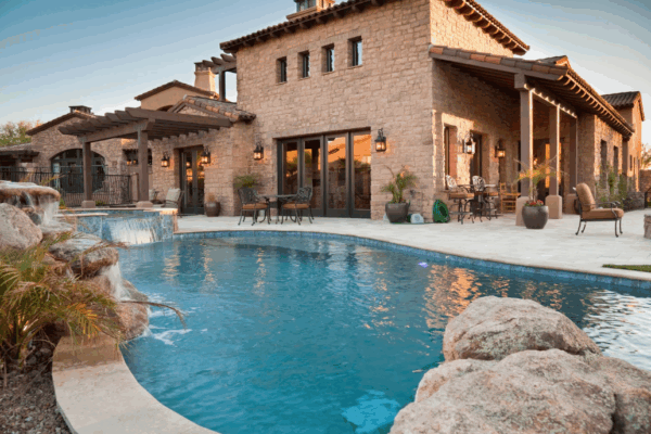 a pool with a luxury stucco home in the background and hardscapes framing it